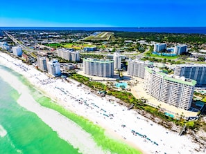 A coastal resort area with beachfront hotels, a swimming pool, and a road leading to the beach.