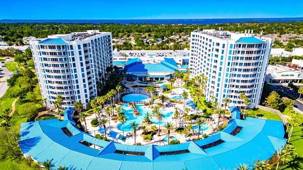 Un resort con dos edificios altos, un área de piscina central y vegetación circundante.