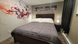 Une chambre d’hôtel avec un grand lit, une tête de lit, une table de chevet avec une lampe et des œuvres d’art abstraites accrochées au mur.