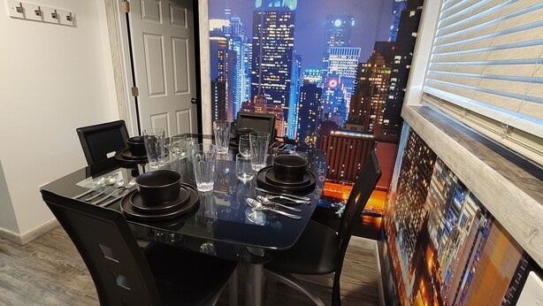 Une table à manger dressée avec de l’argenterie noire, des verres transparents et des couverts, avec une vue sur le paysage urbain par la fenêtre.