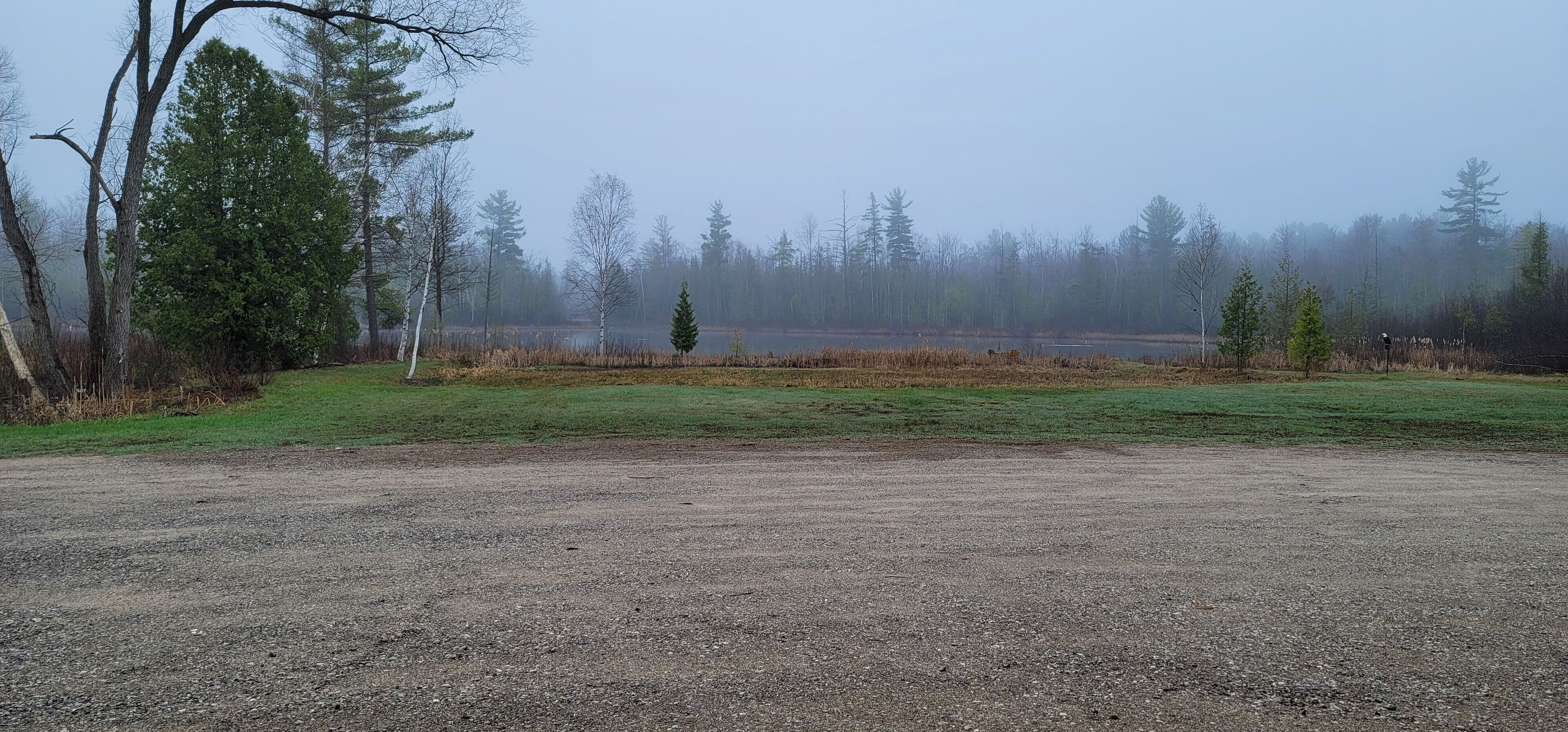 A gravel parking area with a grassy field and trees in the background.