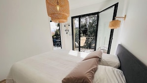 Un dormitorio con una cama grande, una ventana con vistas a muebles de exterior y una lámpara de techo de fibras naturales.