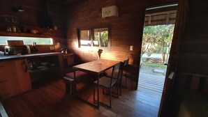 A cozy cabin interior with a wooden dining table, chairs, a kitchen area with a stove, and a window overlooking a natural landscape. - PEACE AND NATURE AT ITS BEST BEACH, HERE IN URUGUAY (La Pedrera)