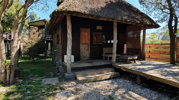 A rustic cabin with a thatched roof, wooden exterior, and a porch with benches. - PEACE AND NATURE AT ITS BEST BEACH, HERE IN URUGUAY (La Pedrera)