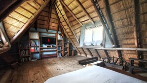 A cozy attic bedroom with a sloped wooden ceiling, a bed, a TV, and bookshelves. - PEACE AND NATURE AT ITS BEST BEACH, HERE IN URUGUAY (La Pedrera)