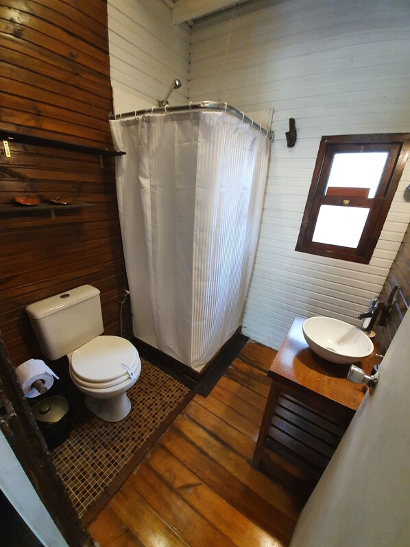 A bathroom with a wooden floor, a white toilet, a shower with a white curtain, and a wooden vanity with a sink.