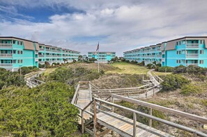 Et hotel ved stranden med flere blå bygninger, træpromenader og en flagstang.