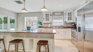 A kitchen with white cabinets, a stainless steel refrigerator, and two bar stools. - -Sea Coast Living At it's BEST, Heated pool, near beaches, shops, restaurants (Naples)