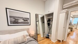 A bedroom with a bed, a bedside table with a lamp, a framed picture on the wall, a wardrobe, and an open door leading to a bathroom. - Charming Hoboken location. Fast Path, Bus or Ferry to NYC.  High End Furniture.  (Hoboken)
