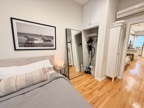 A bedroom with a bed, a bedside table with a lamp, a framed picture on the wall, a wardrobe, and an open door leading to a bathroom.