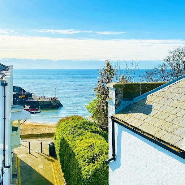 A coastal view with a clear sky, a dock with boats, and a white building with a tiled roof.