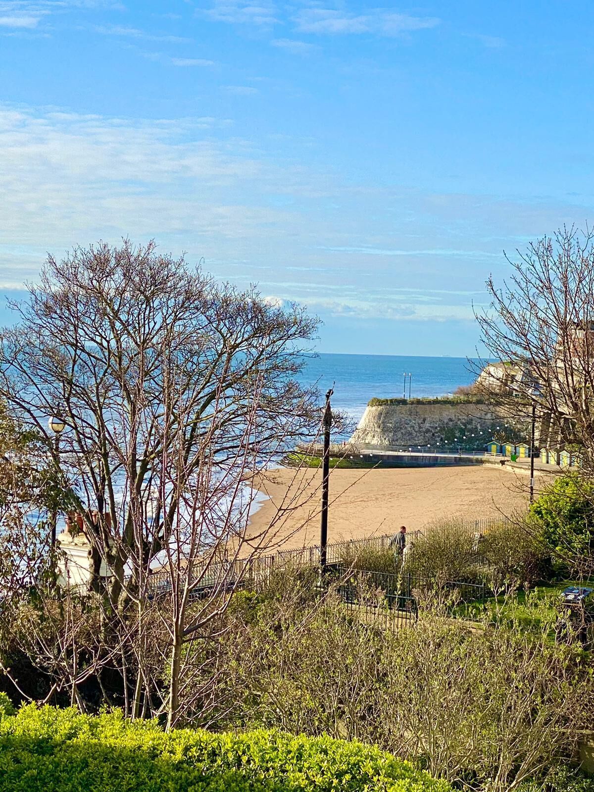 A coastal view with a sandy beach, a rocky outcrop, and sparse vegetation.