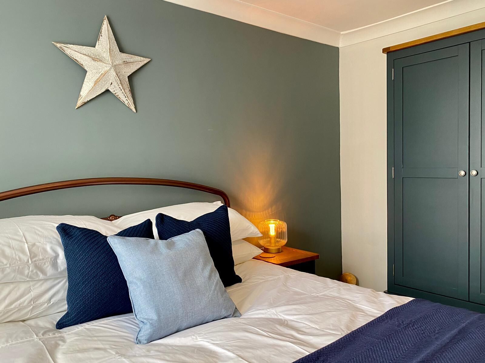 Un llit ben fet amb una decoració d'estreles, una làmpada de nit i un armari en una habitació de disseny senzill i net.