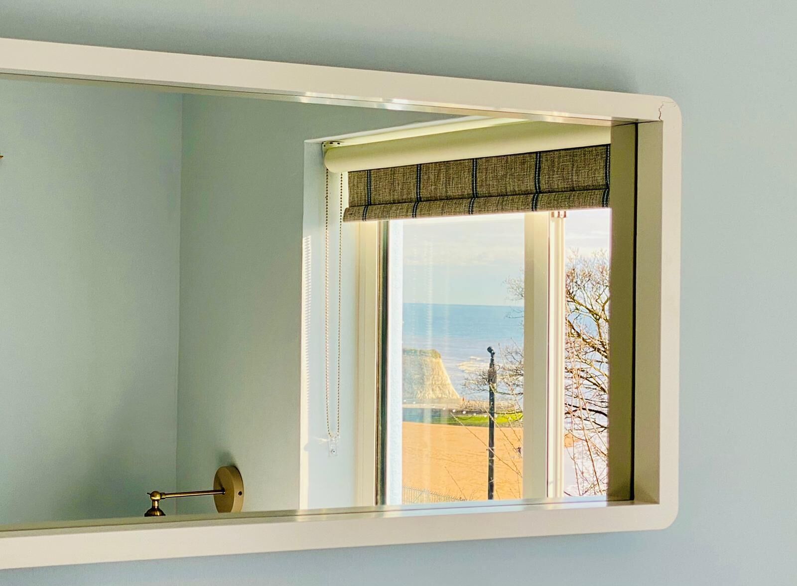 A room with a large window, a visible door handle, and a view of a beach and a building.