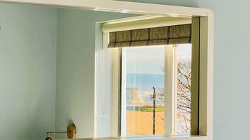 A room with a large window, a visible door handle, and a view of a beach and a building.