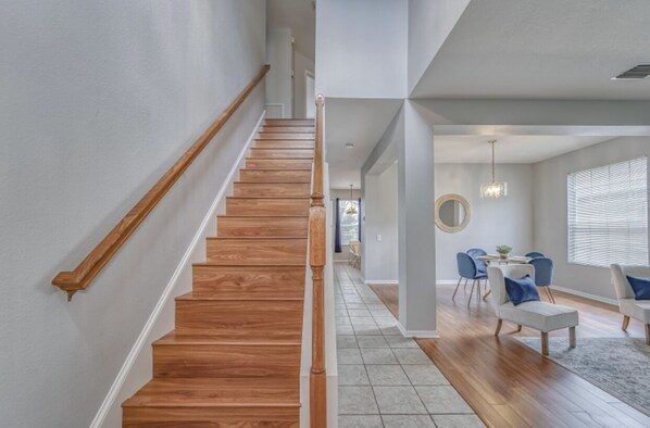 A staircase with wooden steps and a handrail, leading to a dining area with a table and chairs.