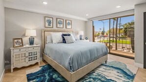 A bedroom with a large bed, a nightstand with a lamp, a dresser, and a view of the outside. - Updated 3-Bedroom Getaway in Coronado Village (Coronado)