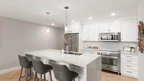 A modern kitchen with white cabinets, stainless steel appliances, and a marble island with bar stools. - Updated 3-Bedroom Getaway in Coronado Village (Coronado)