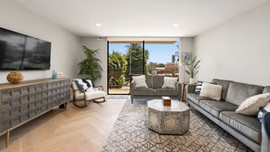 A modern living room with a grey sofa, a patterned rug, and a flat-screen TV on a cabinet. - Updated 3-Bedroom Getaway in Coronado Village (Coronado)