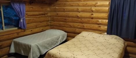 A cabin room with two beds, wooden walls, a window with curtains, and a carpeted floor.