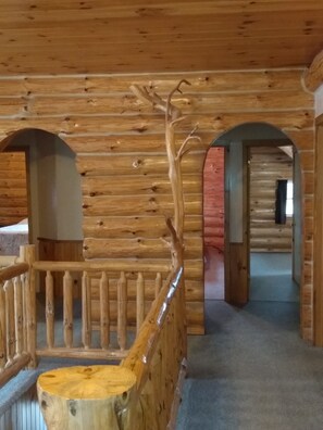 A wooden interior with a staircase, wooden railings, and a view into another room.