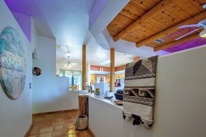 Un couloir avec un plafond en bois, un grand tableau, un tapis tissé et une vue sur un espace cuisine.