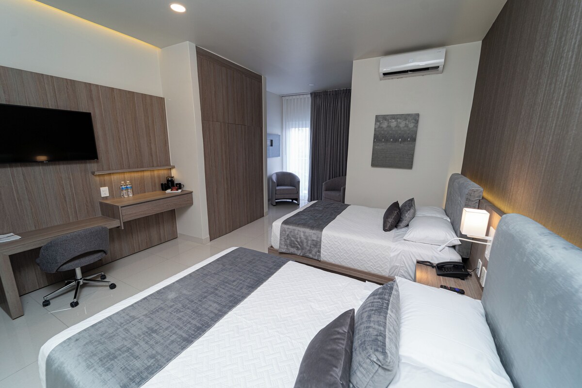 A hotel room with two beds, a desk, a chair, a TV, and a window with curtains.