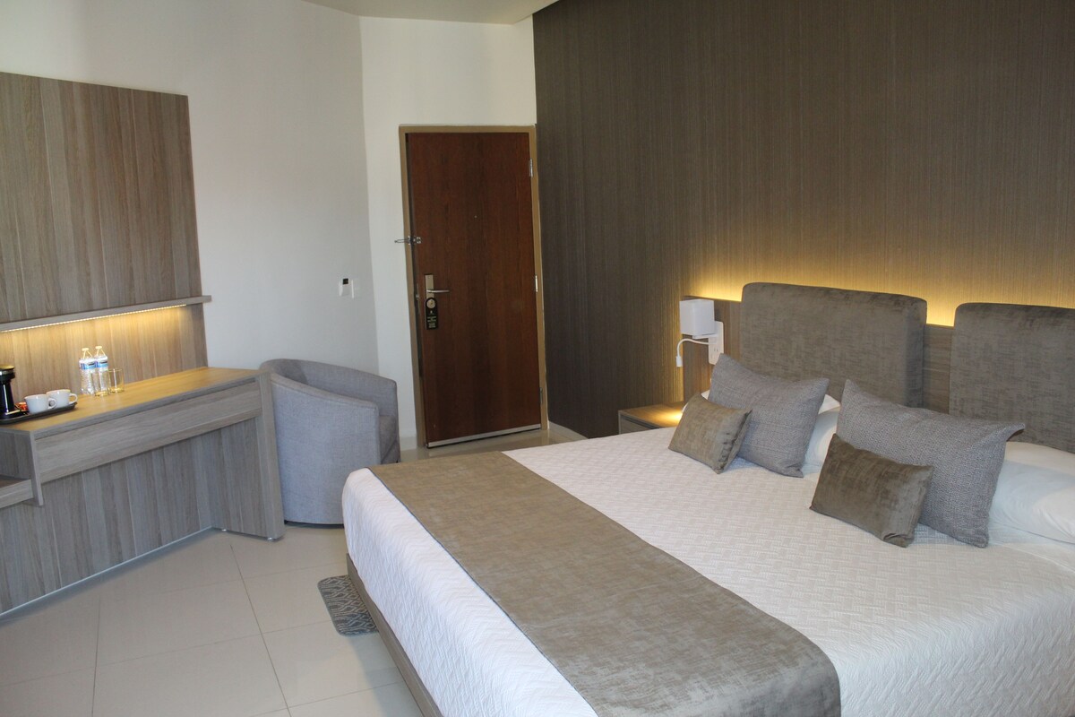 A hotel room with a bed, bedside table, lamp, and a door.
