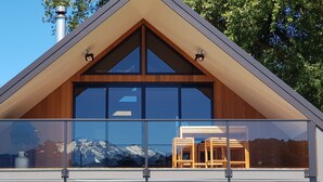 Un edificio moderno con techo triangular, ventanas grandes y un balcón con mobiliario de madera.