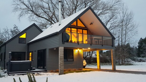 Una casa moderna de dos pisos con balcón, ventanas amplias y una chimenea visible.