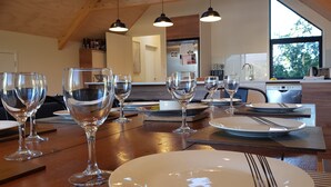 Un comedor con mesas de madera, vasos transparentes y vistas a la cocina y al exterior.
