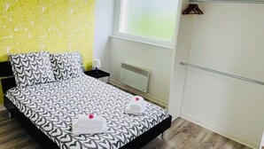 A bedroom with a patterned bedspread, a window with blinds, a radiator, and a wardrobe. - Agréable Appartement sur les Hauteurs de Quimperlé (Quimperlé)