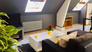 A modern loft apartment with skylights, a flat-screen TV, a white coffee table, a brown sofa, and a small plant. - Agréable Appartement sur les Hauteurs de Quimperlé (Quimperlé)