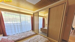 Ein Hotelzimmer mit zwei Betten, einem großen Spiegel und Blick ins Freie durch transparente Vorhänge.
