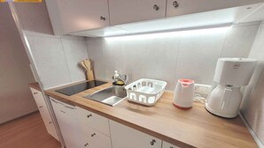 Eine kleine Küche mit Spüle, Kaffeemaschine und einer Körbe auf der Arbeitsfläche.