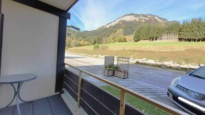 Ein Balkon mit Bergblick, ein geparktes Auto davor und ein kleiner Tisch mit einem Stuhl.