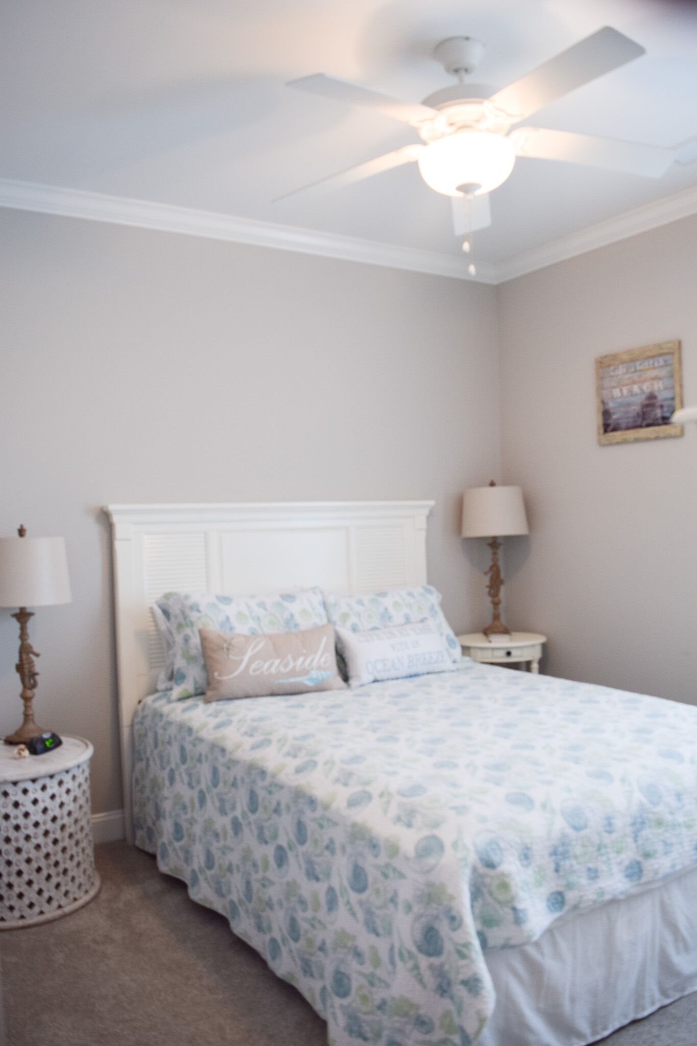 A bedroom with a bed, a ceiling fan, a nightstand with a lamp, and a wall-mounted picture.