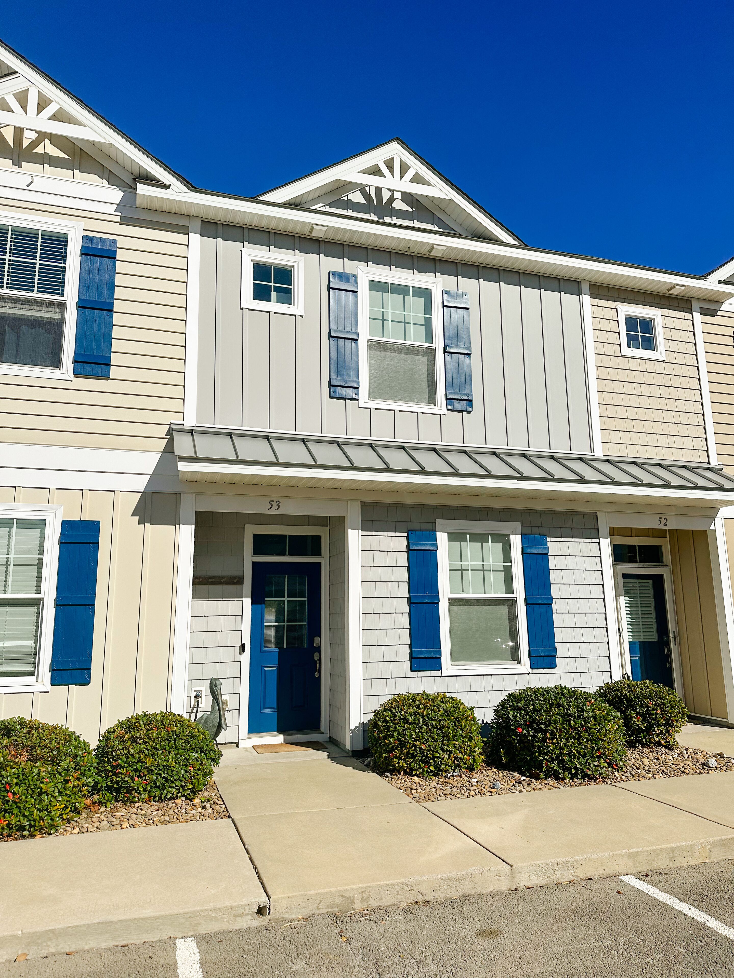 A two-story building with a beige exterior, blue shutters, and a white front door.