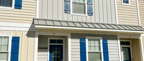 A two-story building with a beige exterior, blue shutters, and a white front door.