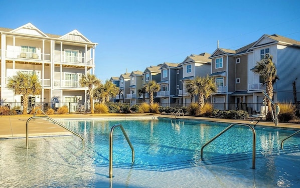 A swimming pool surrounded by multi-story residential buildings with balconies and palm trees.