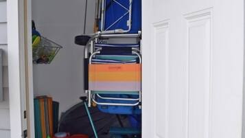 Zona d'emmagatzematge amb una porta blanca, que conté diversos objectes com una cadira plegable blava, un estriatge blau i una cistella verda.