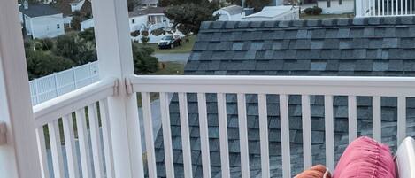 A covered porch with a wooden deck, a pink cushioned bench, and a view of houses and trees under a sunset sky.