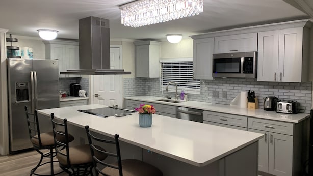 A modern kitchen with a large island, stainless steel appliances, and a chandelier. - Cozy 5 Bedroom 85” TV Home in a Secluded Area (Jacksonville)