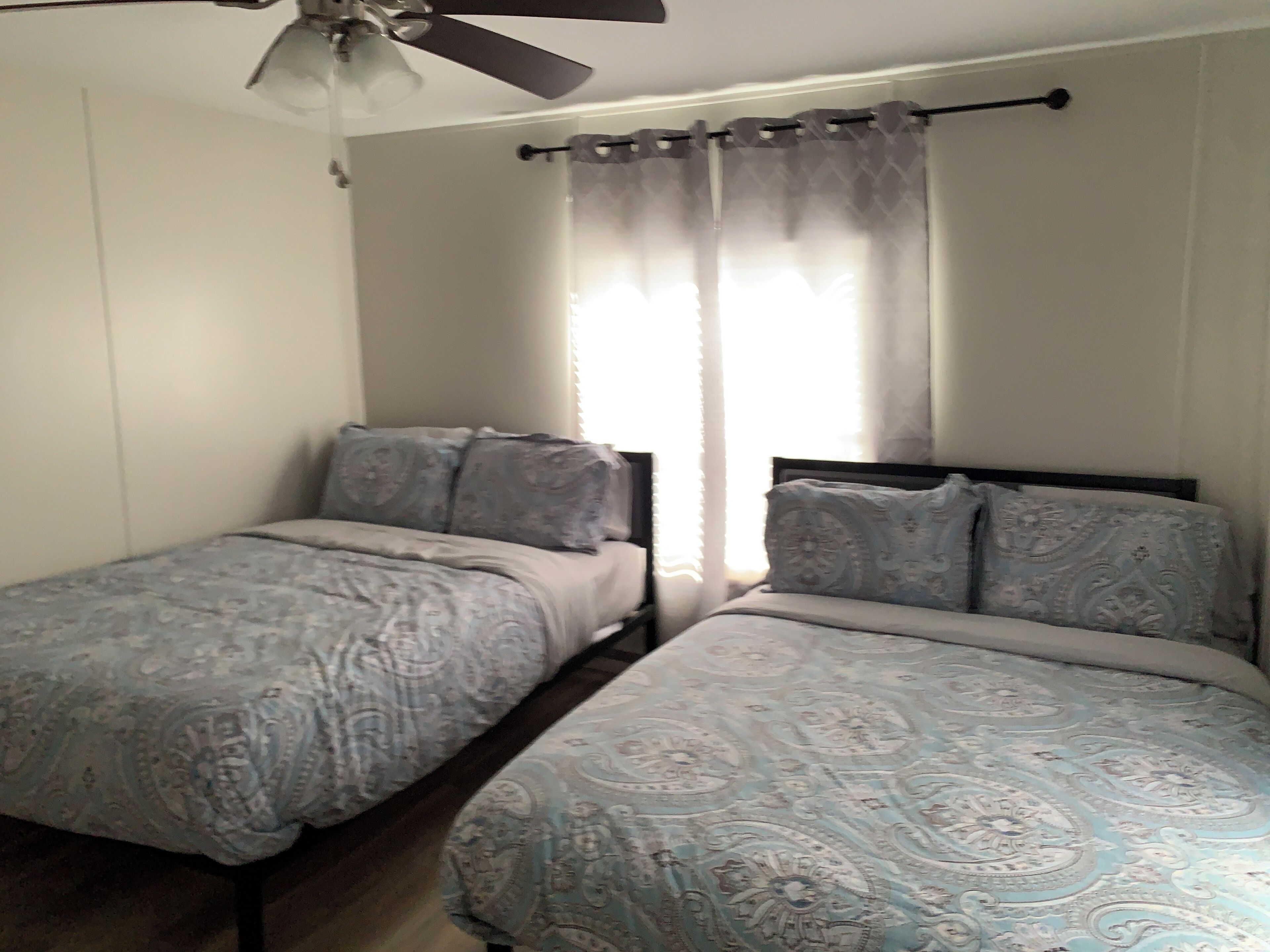 Une chambre avec deux lits simples, un ventilateur de plafond et une fenêtre avec des rideaux légers.