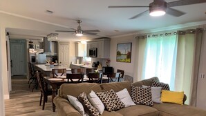 A living room with a sectional sofa, a dining area with a kitchen in the background, and a ceiling fan. - Cozy 5 Bedroom 85” TV Home in a Secluded Area (Jacksonville)