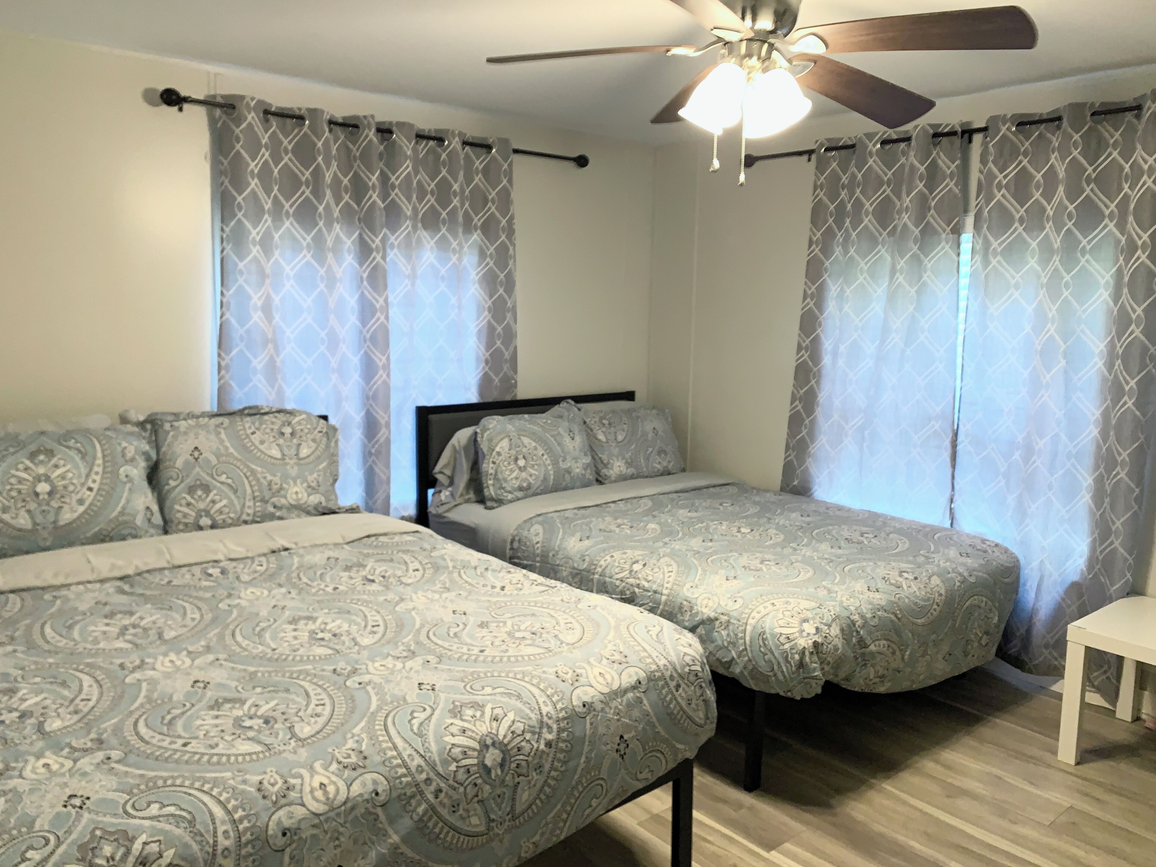 A bedroom with two beds, patterned bedding, a ceiling fan, and curtains.