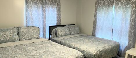 A bedroom with two beds, patterned bedding, a ceiling fan, and curtains.