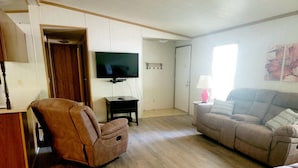 A living room with a brown leather armchair, a beige sofa, a television on a stand, and a small table with a lamp.