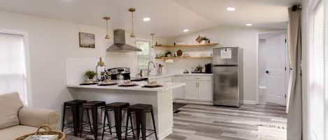 A modern kitchen with a central island, bar stools, and a refrigerator.