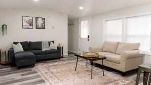 Un soggiorno con un divano grigio, un divano beige, un tappeto decorato e un tavolino con un cesto.